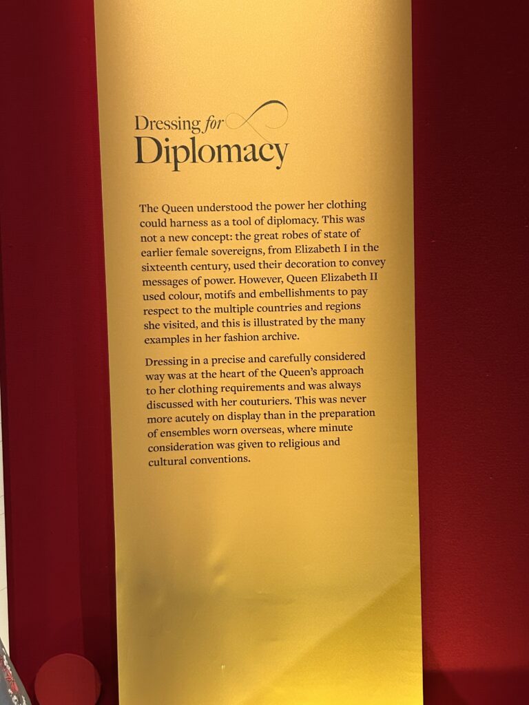 A marker at the exhibition states: Dressing for Diplomacy
The Queen understood the power her clothing could harness as a tool of diplomacy. This was not a new concept: the great robes of state of earlier female sovereigns, from Elizabeth I in the sixteenth century, used their decoration to convey messages of power. However, Queen Elizabeth II used colour, motifs and embellishments to pay respect to the multiple countries and regions she visited, and this is illustrated by the many examples in her fashion archive.
Dressing in a precise and carefully considered way was at the heart of the Queen's approach to her clothing requirements and was always discussed with her couturiers. This was never more acutely on display than in the preparation of ensembles worn overseas, where minute consideration was given to religious and cultural conventions.