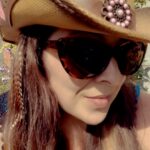 Woman wearing cowboy hat, sunglasses, and hair feathers.