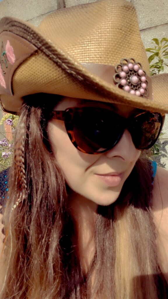 Woman wearing cowboy hat, sunglasses, and hair feathers.